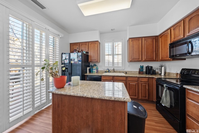 kitchen with black appliances, light hardwood / wood-style floors, sink, a kitchen island, and a healthy amount of sunlight