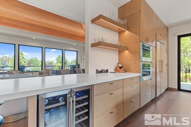 kitchen featuring dark wood-type flooring, stainless steel double oven, beverage cooler, and light brown cabinetry