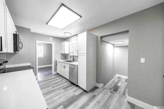 kitchen with appliances with stainless steel finishes, white cabinetry, tasteful backsplash, sink, and light hardwood / wood-style flooring