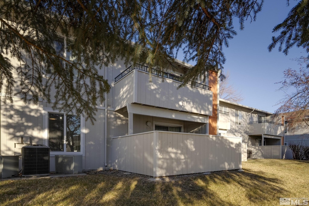 back of house with a balcony, central AC unit, and a yard