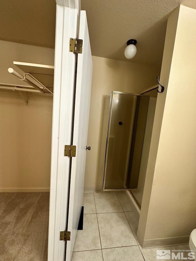 bathroom with toilet, a shower with door, a textured ceiling, and tile patterned floors