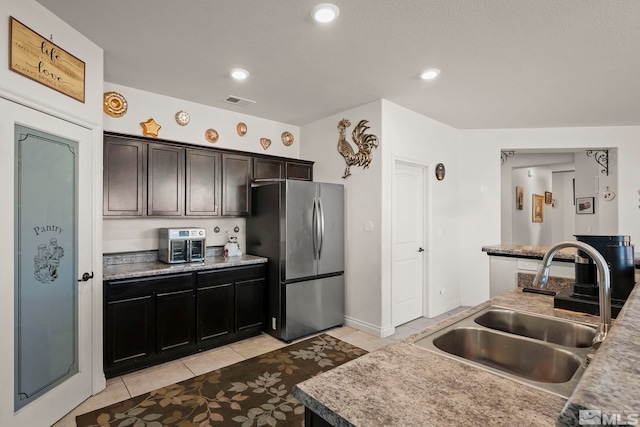 kitchen featuring sink, light tile patterned flooring, dark brown cabinets, and stainless steel refrigerator