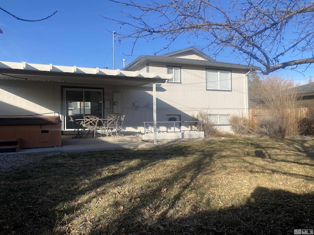 back of house featuring a hot tub, a lawn, and a patio