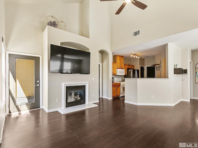 unfurnished living room with a towering ceiling, ceiling fan, and dark hardwood / wood-style flooring