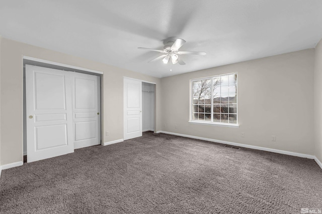 unfurnished bedroom with dark colored carpet, two closets, and ceiling fan