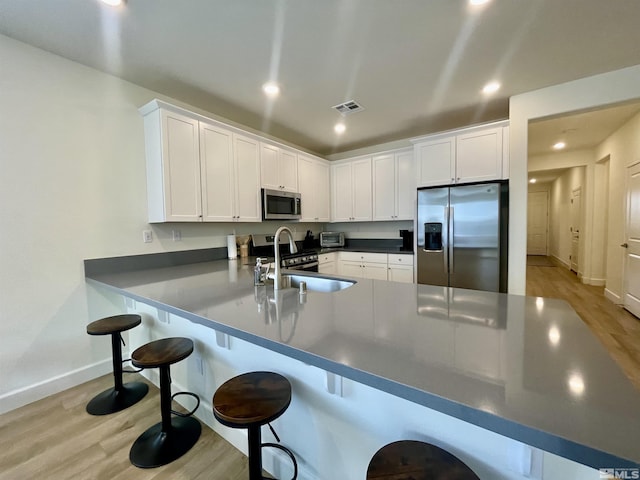 kitchen with a kitchen bar, appliances with stainless steel finishes, white cabinets, sink, and kitchen peninsula