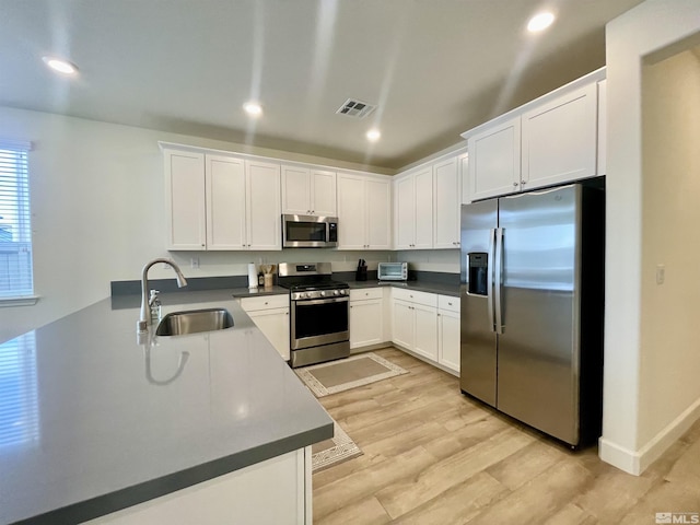 kitchen with sink, stainless steel appliances, white cabinetry, and light hardwood / wood-style floors