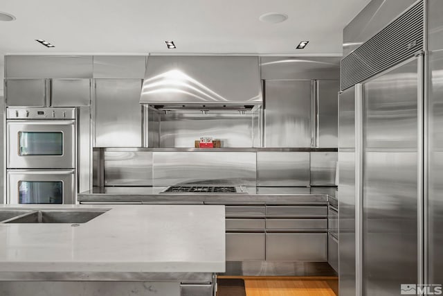 kitchen with light stone countertops, appliances with stainless steel finishes, sink, gray cabinets, and range hood