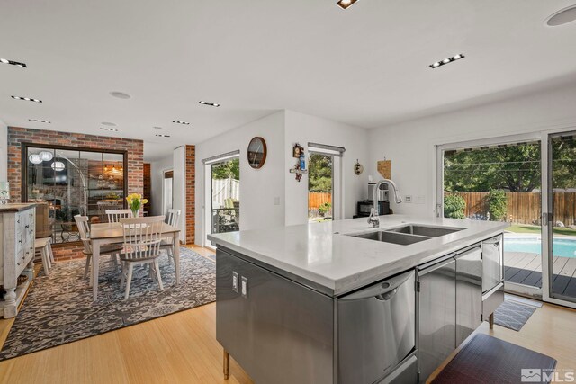 kitchen featuring stainless steel dishwasher, sink, light wood-type flooring, and an island with sink