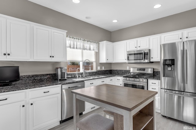 kitchen featuring appliances with stainless steel finishes, white cabinets, dark stone countertops, sink, and light hardwood / wood-style flooring