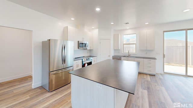 kitchen with white cabinets, appliances with stainless steel finishes, a center island, and light hardwood / wood-style flooring