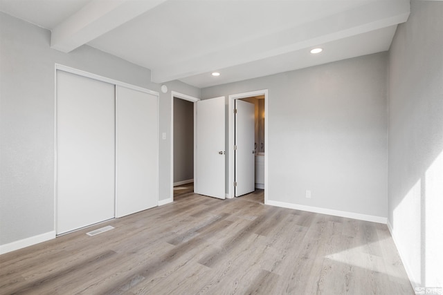 unfurnished bedroom with beamed ceiling, light hardwood / wood-style floors, and a closet