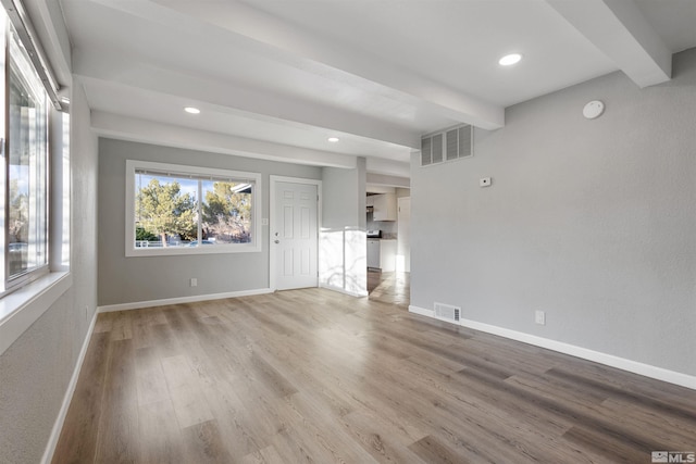 unfurnished living room featuring light wood-type flooring and beam ceiling