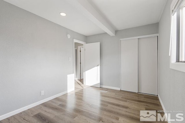 unfurnished bedroom with beam ceiling, light hardwood / wood-style floors, and a closet