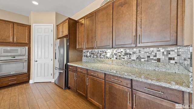 kitchen featuring tasteful backsplash, light stone countertops, appliances with stainless steel finishes, and light wood-type flooring