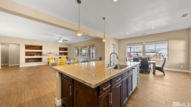 kitchen featuring sink, a kitchen island with sink, light stone countertops, built in shelves, and decorative light fixtures