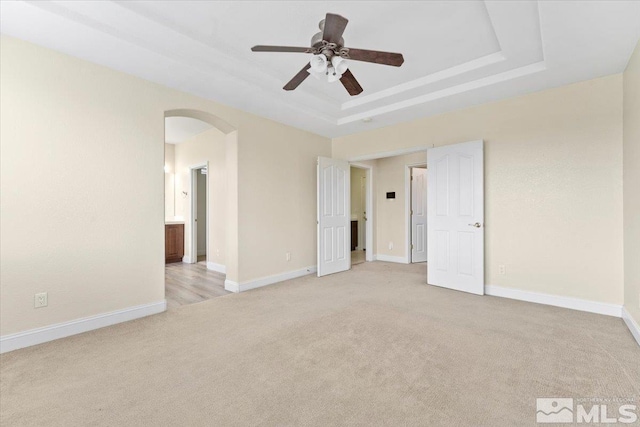 unfurnished bedroom featuring light colored carpet, a raised ceiling, and ceiling fan