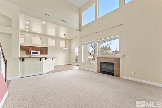 unfurnished living room with light colored carpet, a tile fireplace, and a high ceiling