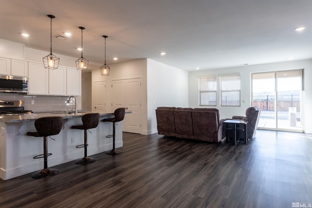 kitchen with a breakfast bar area, dark stone countertops, hanging light fixtures, white cabinetry, and stainless steel appliances