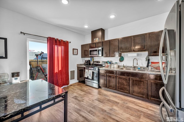 kitchen with sink, stainless steel appliances, dark brown cabinetry, light hardwood / wood-style floors, and dark stone counters