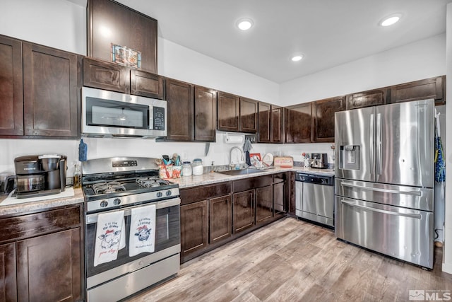 kitchen featuring sink, light stone counters, stainless steel appliances, dark brown cabinets, and light wood-type flooring