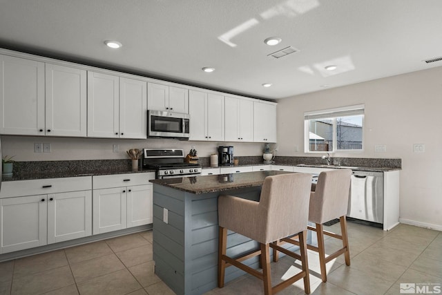 kitchen with light tile patterned floors, stainless steel appliances, a kitchen breakfast bar, white cabinets, and a kitchen island