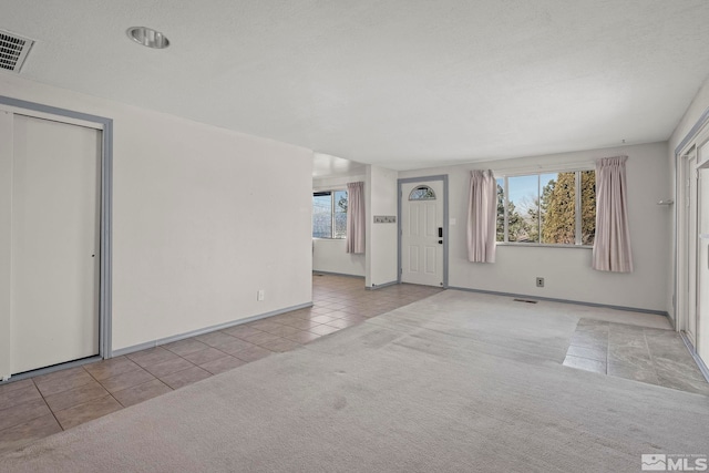 empty room with light tile patterned flooring, a textured ceiling, and a wealth of natural light