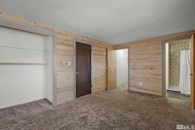 unfurnished bedroom featuring connected bathroom, wooden walls, and dark colored carpet