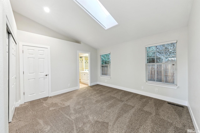 unfurnished bedroom featuring a closet, ensuite bathroom, vaulted ceiling with skylight, and carpet