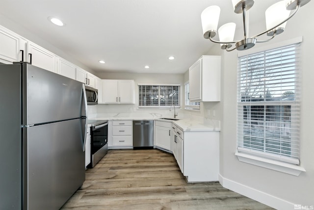 kitchen featuring sink, pendant lighting, stainless steel appliances, light hardwood / wood-style floors, and white cabinets