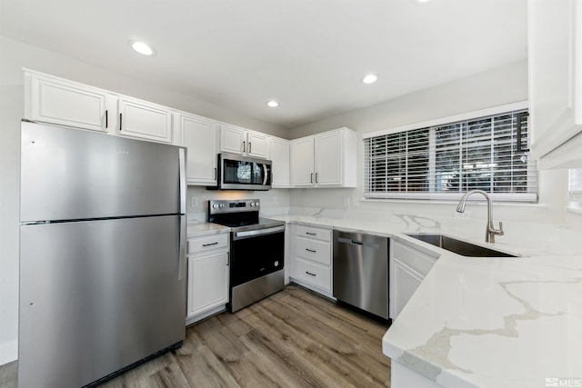 kitchen with sink, appliances with stainless steel finishes, light stone countertops, light hardwood / wood-style floors, and white cabinets