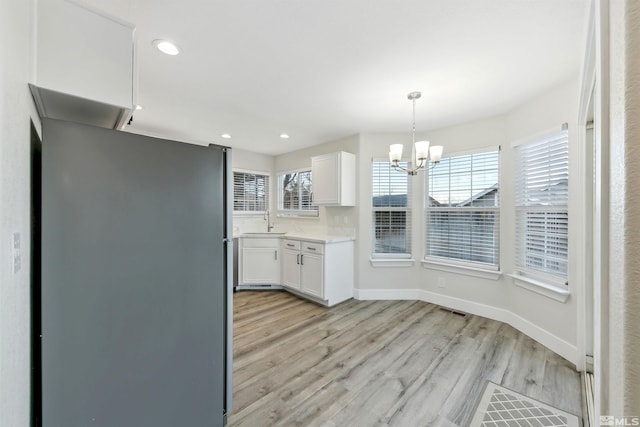 kitchen featuring sink, hanging light fixtures, light wood-type flooring, a notable chandelier, and white cabinets