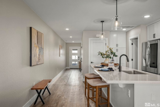 kitchen featuring decorative light fixtures, sink, white cabinets, stainless steel fridge, and light hardwood / wood-style floors