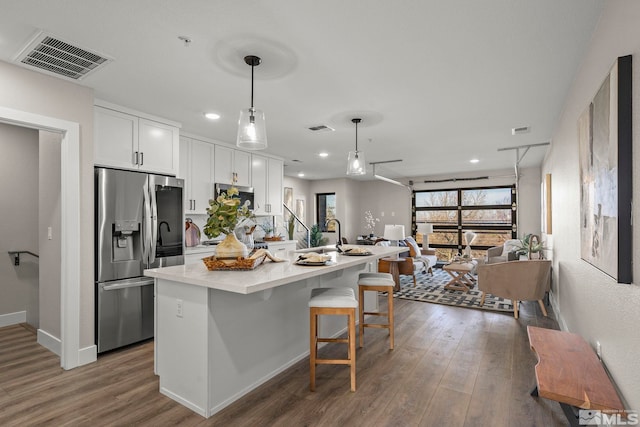 kitchen featuring white cabinetry, hanging light fixtures, a kitchen breakfast bar, stainless steel refrigerator with ice dispenser, and an island with sink