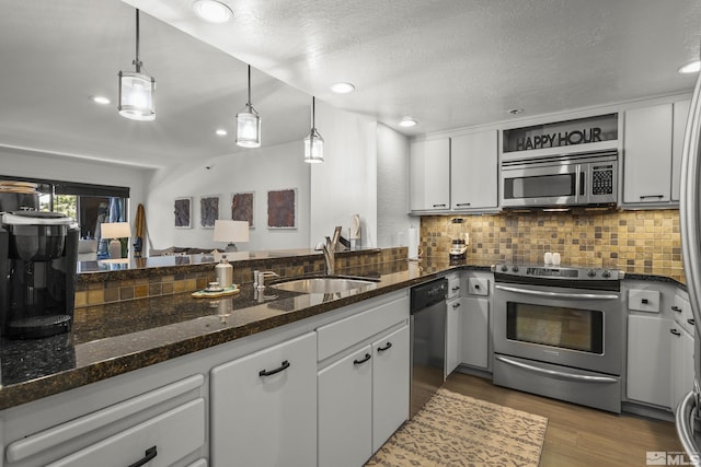 kitchen featuring sink, white cabinetry, hanging light fixtures, stainless steel appliances, and dark stone counters