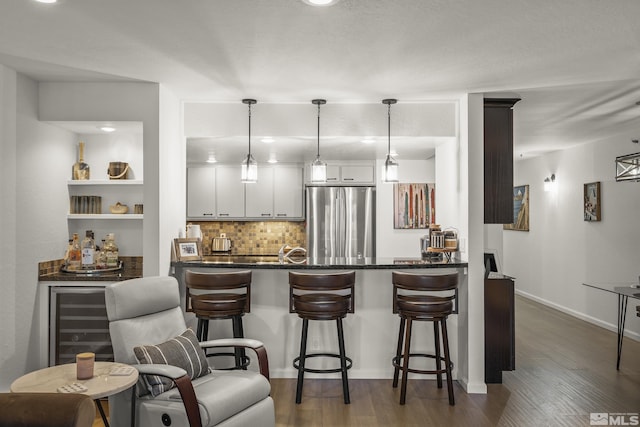 kitchen featuring hanging light fixtures, stainless steel fridge, dark hardwood / wood-style flooring, decorative backsplash, and white cabinets