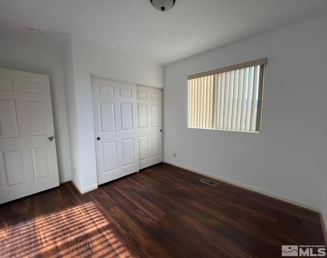 unfurnished bedroom with dark hardwood / wood-style flooring and a closet