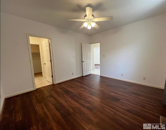 unfurnished bedroom featuring dark hardwood / wood-style flooring, a spacious closet, ceiling fan, and a closet