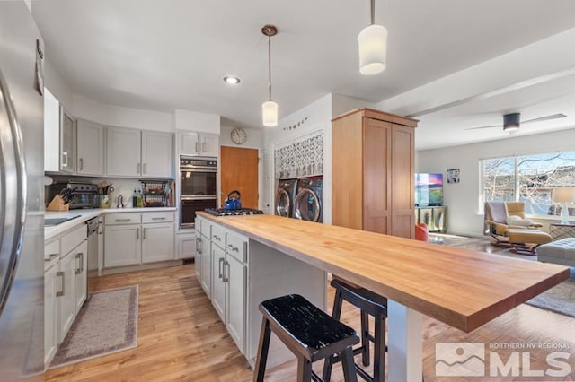 kitchen featuring washing machine and dryer, wooden counters, double oven, and decorative light fixtures