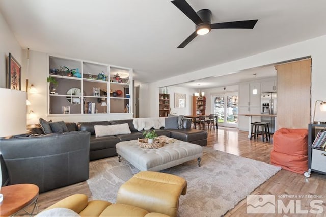 living room featuring ceiling fan with notable chandelier and light wood-type flooring