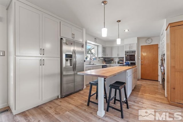 kitchen featuring a kitchen island, wood counters, white cabinetry, stainless steel fridge, and a kitchen bar