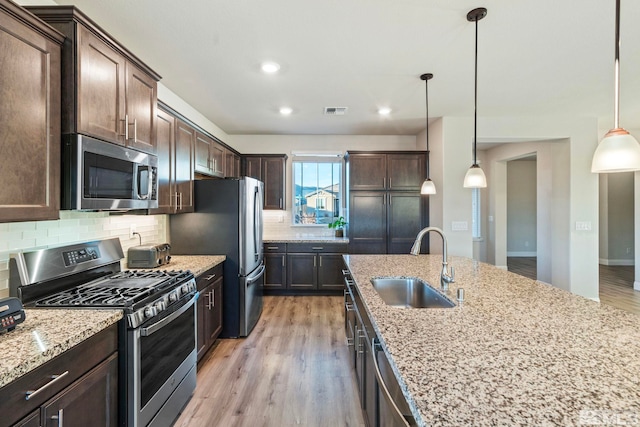 kitchen with sink, backsplash, stainless steel appliances, dark brown cabinetry, and decorative light fixtures