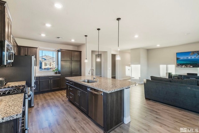 kitchen with appliances with stainless steel finishes, pendant lighting, sink, light stone counters, and a center island with sink