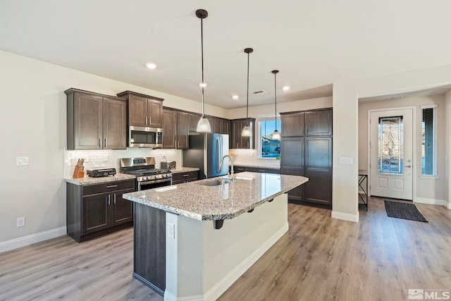 kitchen with sink, light stone counters, decorative light fixtures, stainless steel appliances, and a kitchen island with sink