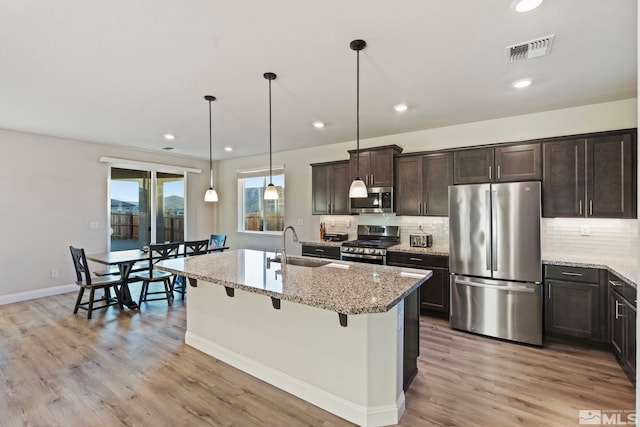 kitchen featuring appliances with stainless steel finishes, pendant lighting, a breakfast bar area, a kitchen island with sink, and light stone countertops