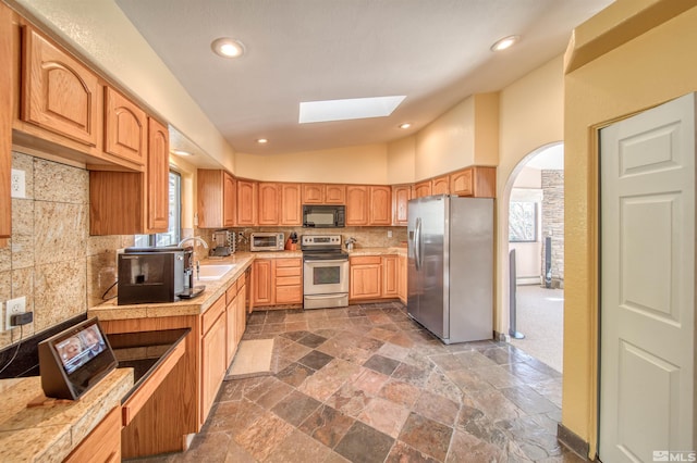 kitchen featuring appliances with stainless steel finishes, high vaulted ceiling, a skylight, sink, and backsplash