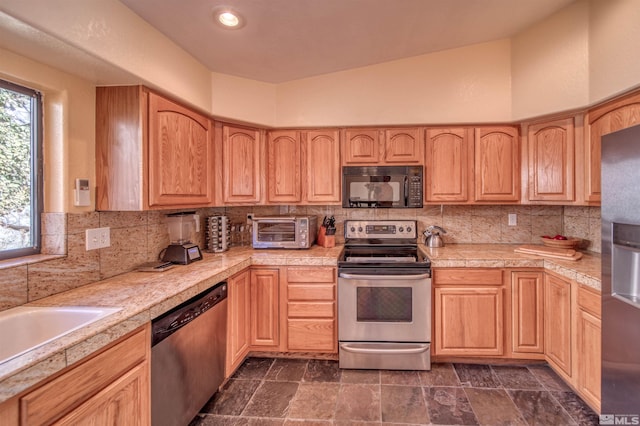 kitchen featuring appliances with stainless steel finishes, lofted ceiling, light brown cabinetry, and decorative backsplash