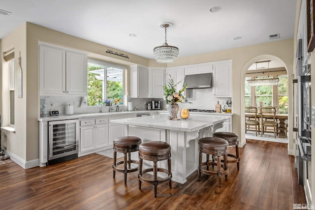 kitchen with wine cooler, extractor fan, white cabinetry, decorative light fixtures, and a kitchen island