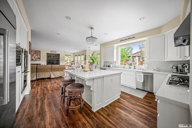 kitchen with white cabinetry, a center island, appliances with stainless steel finishes, pendant lighting, and wall chimney range hood