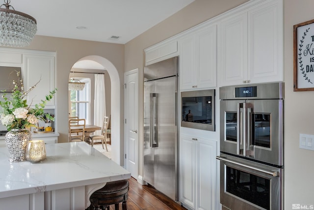 kitchen with white cabinets, a kitchen breakfast bar, hanging light fixtures, built in appliances, and light stone counters